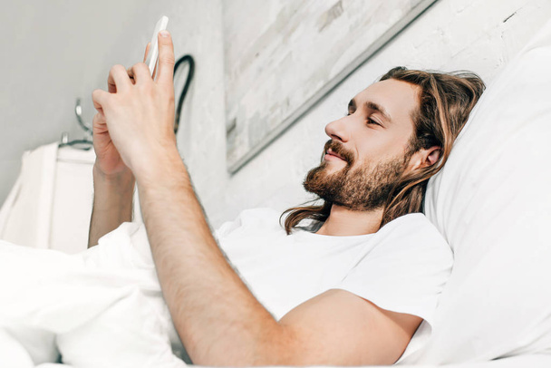 felice Gesù utilizzando lo smartphone a letto durante il mattino a casa
  - Foto, immagini