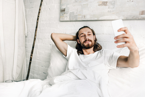 sorrindo Jesus tomando selfie na cama durante o horário da manhã em casa
  - Foto, Imagem