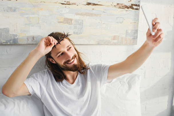 felice Gesù in corona di spine prendendo selfie a letto durante il mattino a casa
  - Foto, immagini