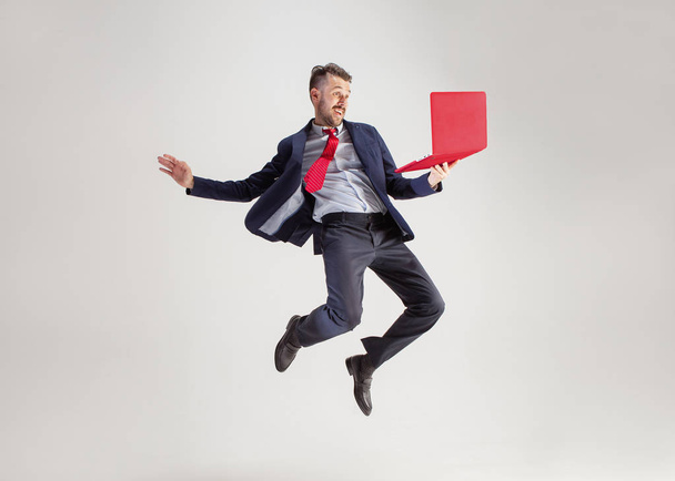 Image of young man over white background using laptop computer while jumping. - Foto, afbeelding
