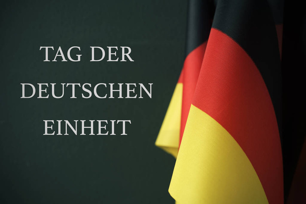 algumas bandeiras da Alemanha e o texto Tag der Deutschen Einheit, Day of German Unity escrito em alemão, contra um fundo verde escuro
 - Foto, Imagem