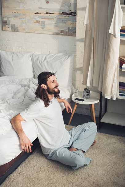 high angle view of smiling Jesus sitting on floor near bed during morning time in bedroom at home  - Fotografie, Obrázek