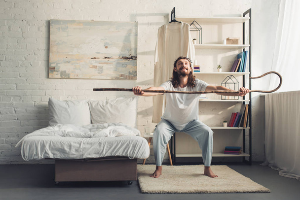 Jésus souriant en couronne d'épines faisant l'entraînement du matin avec le personnel en bois dans la chambre à coucher à la maison
  - Photo, image