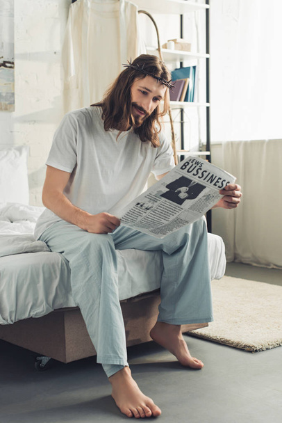 smiling Jesus in crown of thorns reading business newspaper in bedroom during morning time at home - Foto, imagen
