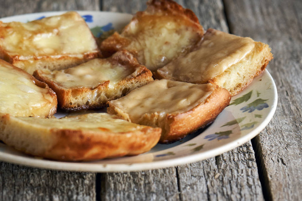 Tostadas con queso derretido en un plato viejo sobre tablas de madera
 - Foto, imagen