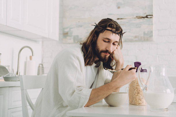 tired Jesus eating corn flakes on breakfast in kitchen at home  - Photo, image
