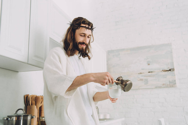 cheerful Jesus pouring coffee from cezve into cup in kitchen during morning time at home  - Foto, Imagem
