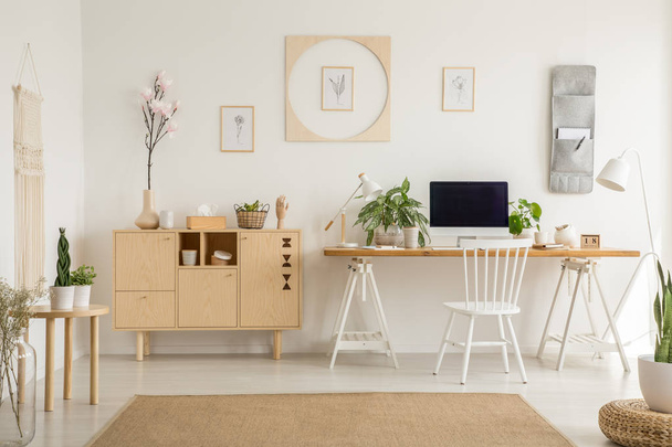 Real photo of a simple home office interior with a cabinet, flower, graphics and desk with a computer. Place your graphic - Photo, Image