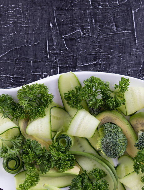 Frisse salade van komkommer, avocado, broccoli en peterselie op zwarte achtergrond. - Foto, afbeelding