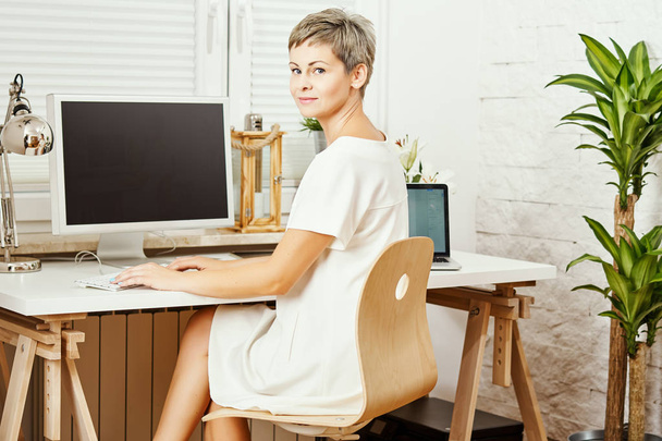 güzel iş kadını masada oturan ve bilgisayarda çalışan beyaz elbiseli - Fotoğraf, Görsel