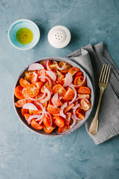 Tasty appetizing tomatoes salad with onions and olives oil in bowl on blue table.  - Foto, Imagem