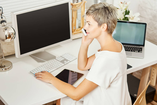 schöne Geschäftsfrau im weißen Kleid sitzt an einem Schreibtisch und telefoniert - Foto, Bild