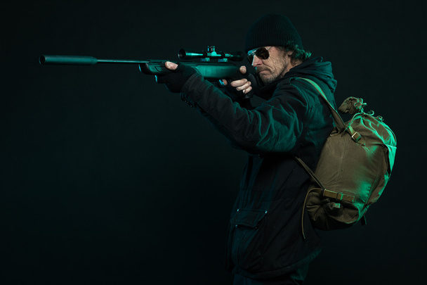 Снайпер с бородой в черном держит пистолет. Снимок студии
. - Фото, изображение