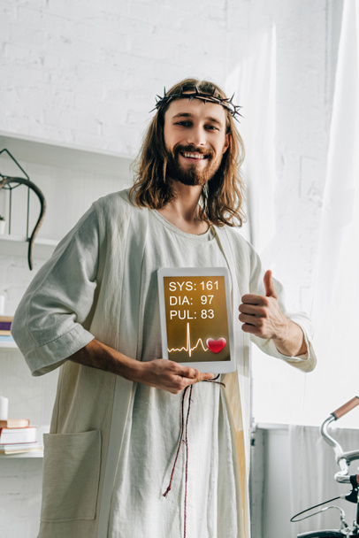 Veselá Ježíše v korunu trnovou dělá gesto palce a zobrazení digitální tablet s lékařské aplikace doma - Fotografie, Obrázek
