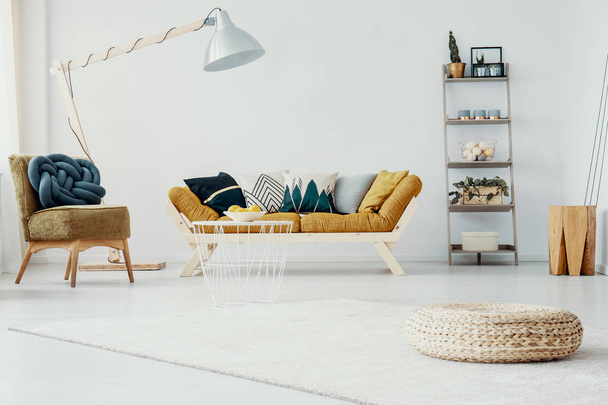 Pouf e sedia in salotto bianco interno con lampada accanto al divano in legno senape. Foto reale
 - Foto, immagini