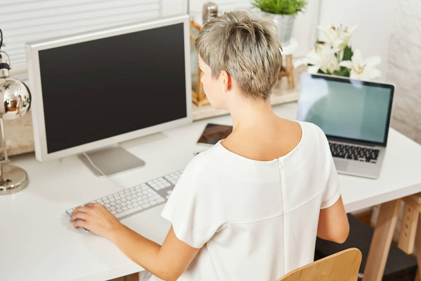 kaunis liike nainen valkoinen mekko istuu pöydällä ja työskentelee tietokoneella
 - Valokuva, kuva