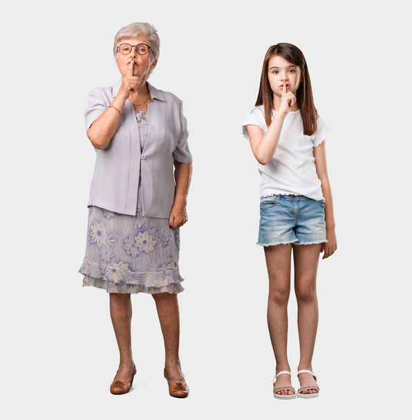 Volledige lichaam van een bejaarde dame en haar kleindochter een geheimhouden of vragend om stilte, ernstige gezicht, gehoorzaamheid concept - Foto, afbeelding