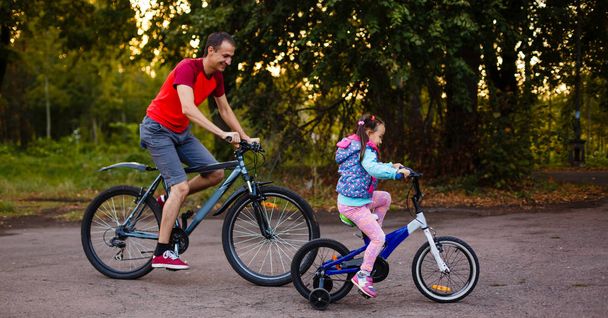 幸せな若い父と緑豊かな公園でバイクに乗って彼は小さな娘 - 写真・画像