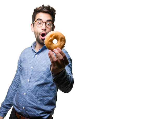 verrast jonge man met een donut geïsoleerd op witte achtergrond - Foto, afbeelding