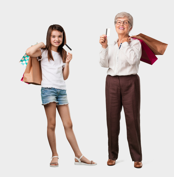 Повне тіло літньої леді та її онуки веселі та усміхнені, дуже схвильовані триманням нової банківської картки та сумки для покупок, готові йти за покупками
 - Фото, зображення