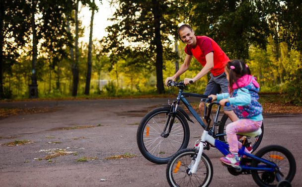mutlu genç baba ve küçük kızı Bisiklet yeşil park, yan görünüm - Fotoğraf, Görsel