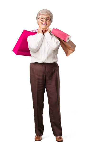 Mujer mayor de cuerpo completo alegre y sonriente, muy emocionada llevando bolsas de compras, lista para ir de compras y buscar nuevas ofertas
 - Foto, Imagen