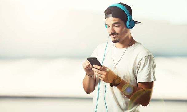 Young rapper man relaxed and concentrated, listening to music with his mobile phone, feeling the rhythm and discovering new artists, eyes closed - Photo, Image