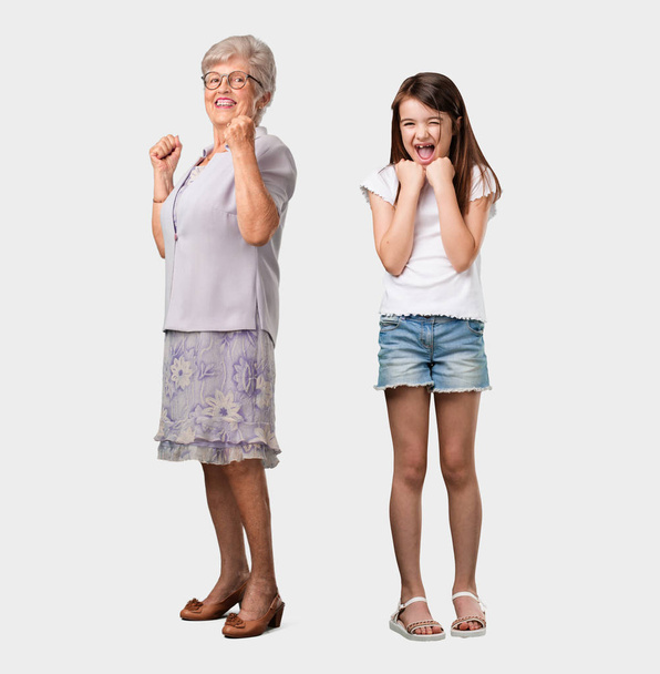 Ganzkörper einer älteren Dame und ihrer Enkelin sehr glücklich und aufgeregt, Arme in die Höhe reckend, einen Sieg oder Erfolg feiernd, Lottogewinn - Foto, Bild