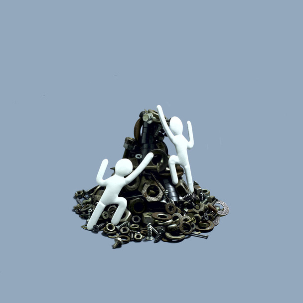 Two paper men climbs up mountain of screw-nuts and bolts. Symbolic image of person's behavior in competition. Strategy to overcome difficulties. Minimal psychological conception - Photo, Image