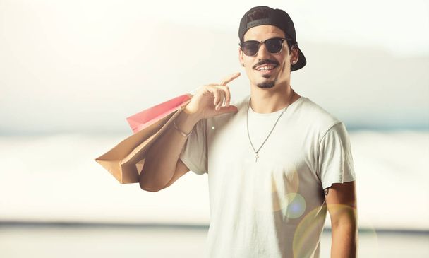 Mladý raper člověk veselý a usmívající se, velmi nadšený, nošení nákupní tašky, jste připraveni jít nakupovat a vyhledávat nové nabídky - Fotografie, Obrázek