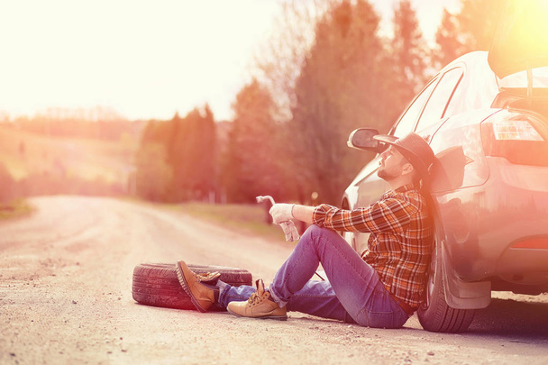 Man is sitting on the road by the car - Zdjęcie, obraz