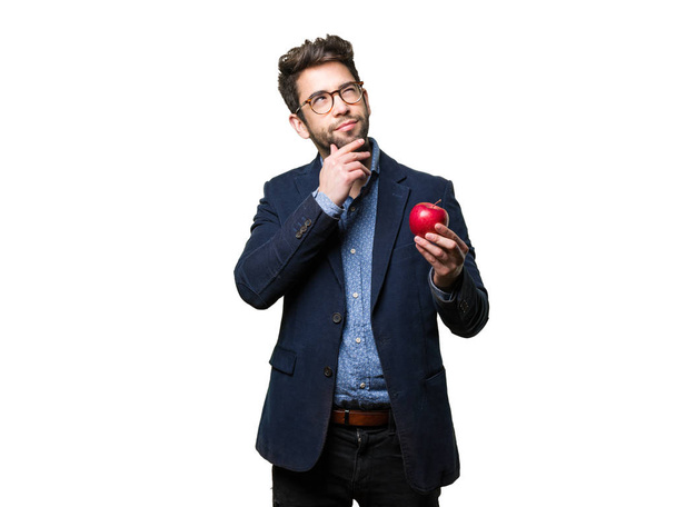 junger Mann denkt und hält einen Apfel isoliert auf weißem Hintergrund - Foto, Bild