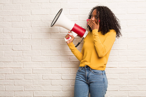 Young black woman with megaphone covering mouth against brick wall - Photo, Image