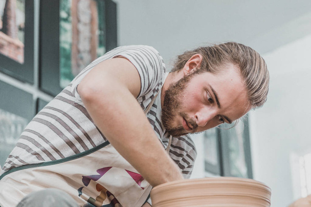 Young pottery artist working on his clay pot in an atelier - Fotografie, Obrázek