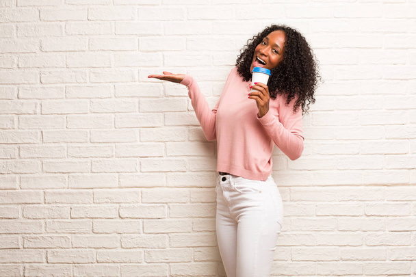 Młody czarny kobieta z jednorazowych coffee cup Rozdziawiony, skoki i dumni przed mur z cegły - Zdjęcie, obraz