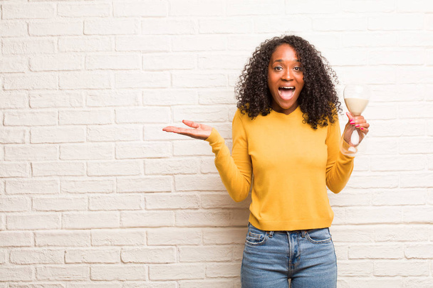 Молода чорна жінка з піщаним склом кричить щасливо, здивована на цегляній стіні
 - Фото, зображення