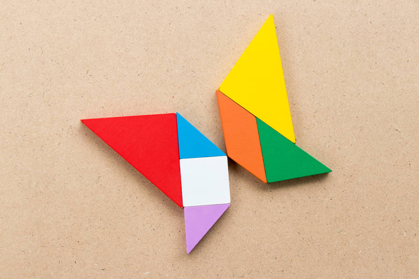 Color tangram puzzle in butterfly shape on wood background - Photo, Image