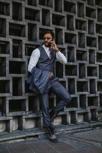 Displeased businessman talking outside on the mobile phone and holding his jacket - Valokuva, kuva