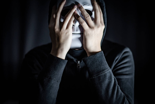 Homem encapuzado misterioso usando máscara branca no quarto escuro. Máscara social anónima. Transtorno depressivo maior ou transtorno bipolar. Conceito de Halloween
 - Foto, Imagem