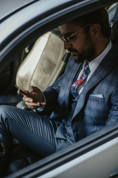 Vakava yrittäjä istuu autossa ja pitelee aurinkolasejaan
 - Valokuva, kuva