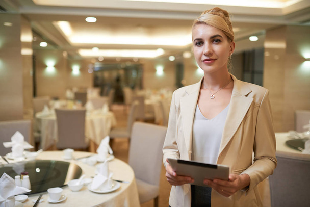 Pretty smiling blonde woman manager in hotel restaurant posing for camera and holding folder  - Фото, зображення