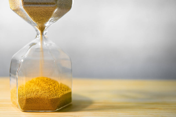 金色の砂は、木製のテーブルにモダンな砂時計の形を実行しています。時間を渡すと時間が不足しています。締め切りのビジネス コンセプトの緊急カウント ダウン タイマー - 写真・画像
