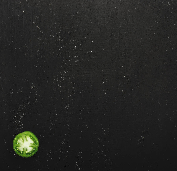 Half a juicy green tomato on a black stone background. Concept of fresh vegetables, top view and copy space - Photo, Image