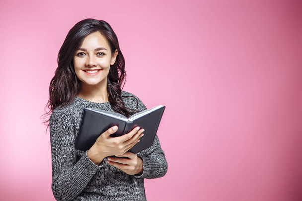 Happy young woman with book on pink background. - Фото, изображение