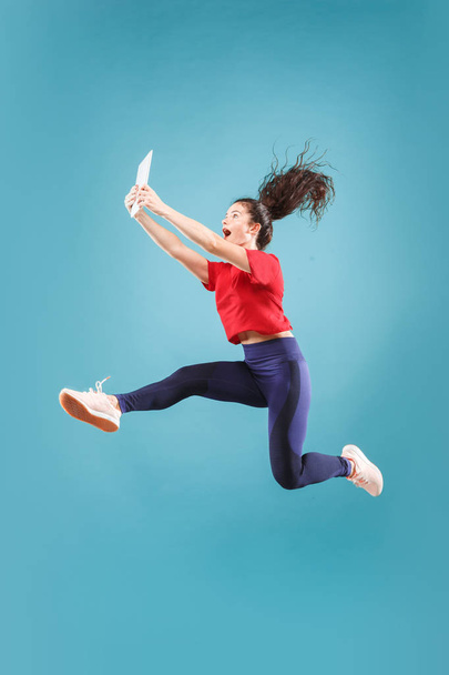 Image of young woman over pink background using laptop computer or tablet gadget while jumping. - Фото, зображення