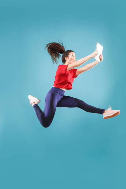 Image of young woman over pink background using laptop computer or tablet gadget while jumping. - Foto, afbeelding