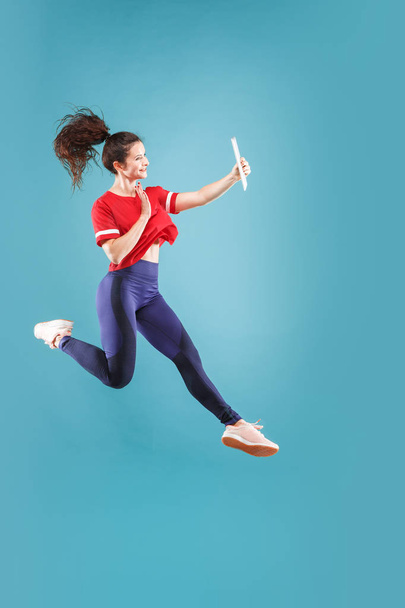 Image of young woman over pink background using laptop computer or tablet gadget while jumping. - Foto, immagini
