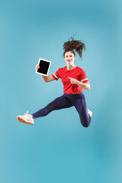Image of young woman over pink background using laptop computer or tablet gadget while jumping. - Fotó, kép