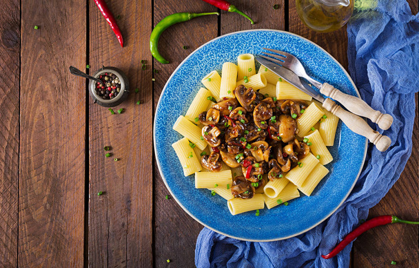 Widok góry pyszne wegetariańskie makaron rigatoni z pieczarkami i papryczki chilli w niebieskie miski na drewnianym stole. - Zdjęcie, obraz