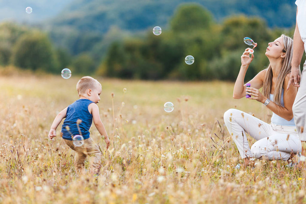 Happy child with family having a great time blowing bubbles outdoors - Φωτογραφία, εικόνα